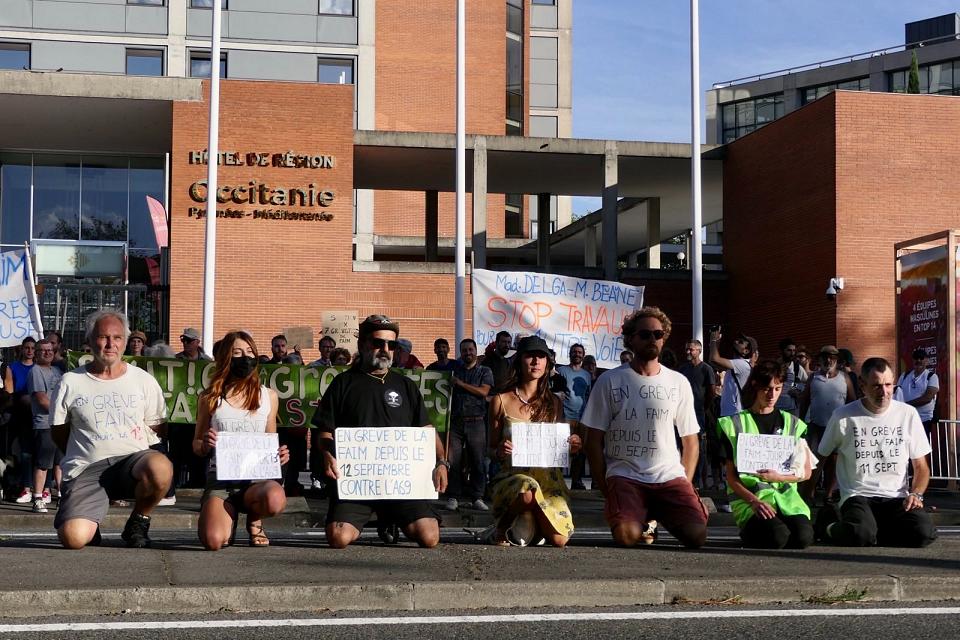 Sept personnes, agenouillées, portent des pancartes "en grève de la faim" devant le conseil régional à Toulouse.