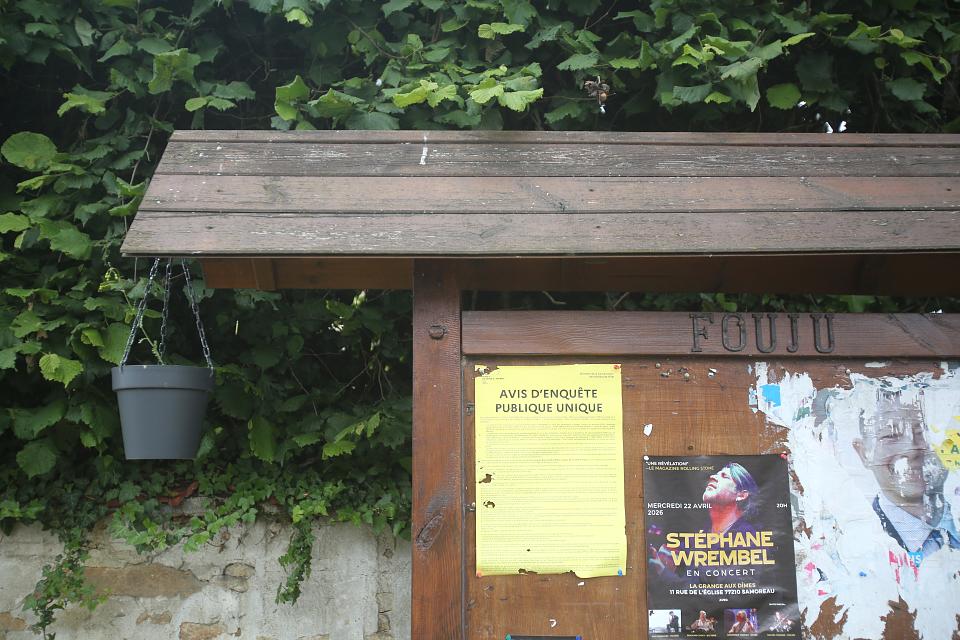 Sur un panneau en bois, une affichette jaune annonce un "avis d'enquête publique". 