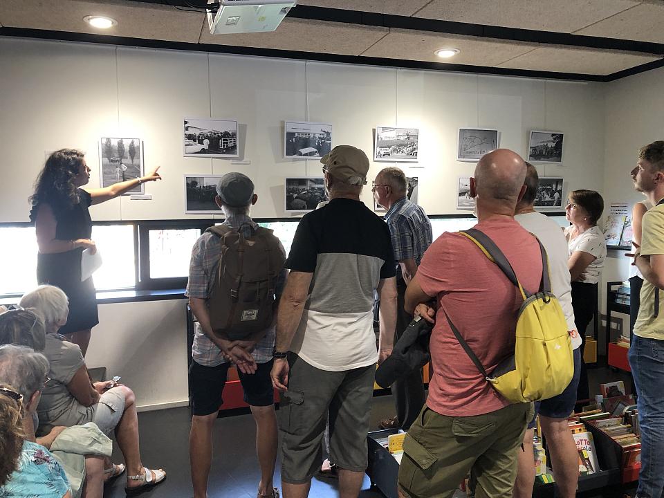 Un groupe d'une douzaine de personnes suit une visite guidée dans une exposition de photos. 