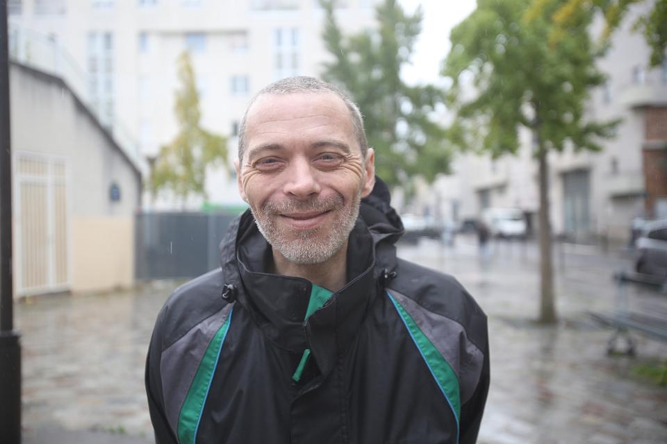 Un homme dehors sous la pluie sourit vers l'objectif. 