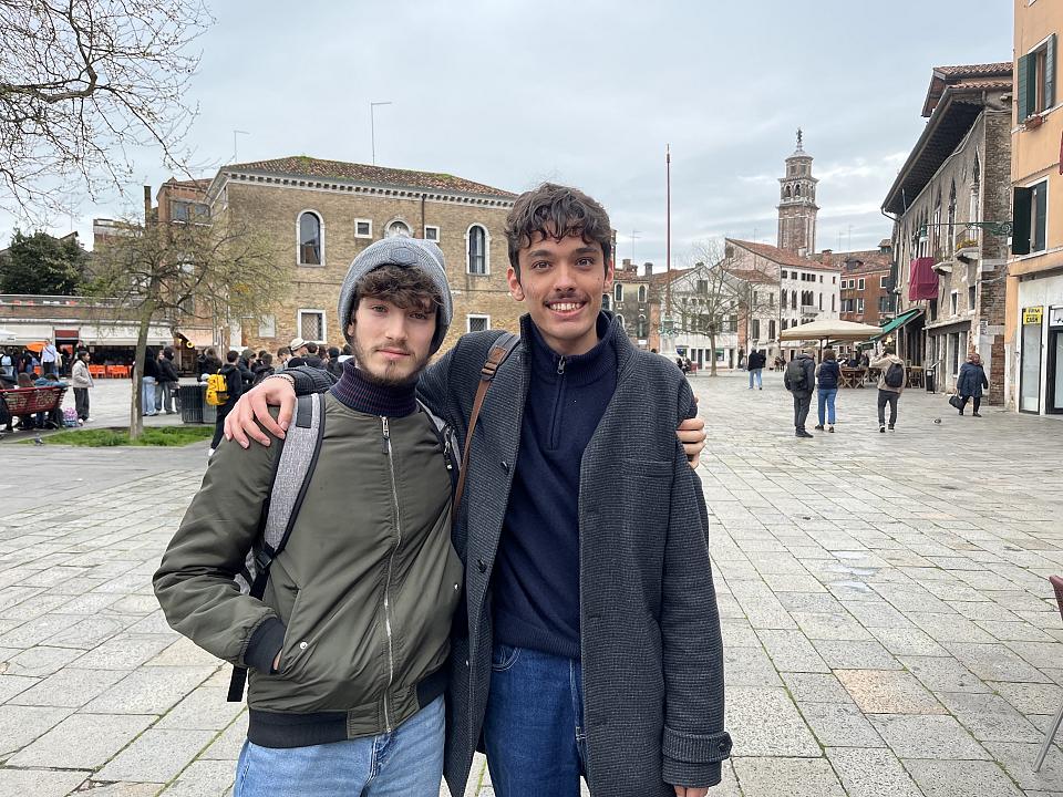 Deux jeunes hommes se tiennent cote-à-cote sur une place à Venise.
