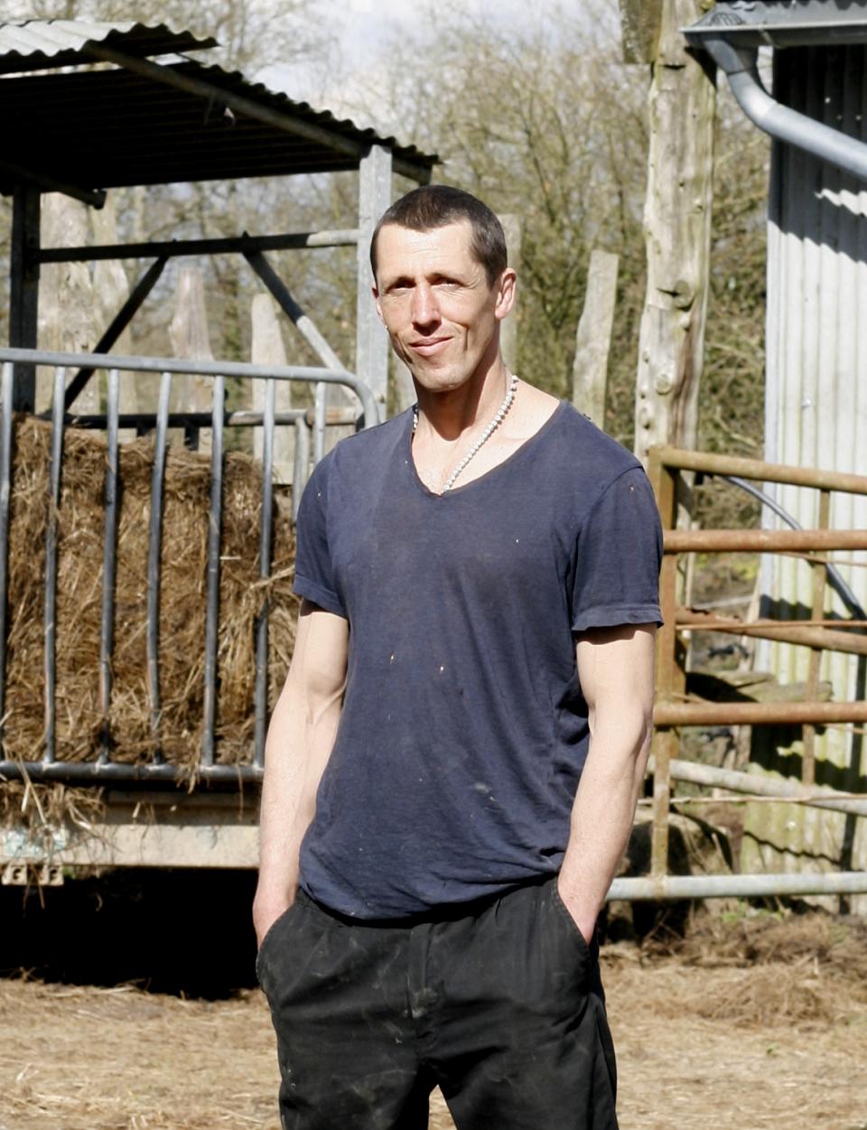 Un homme souriant en t-shirt debout dehors devant du foin.