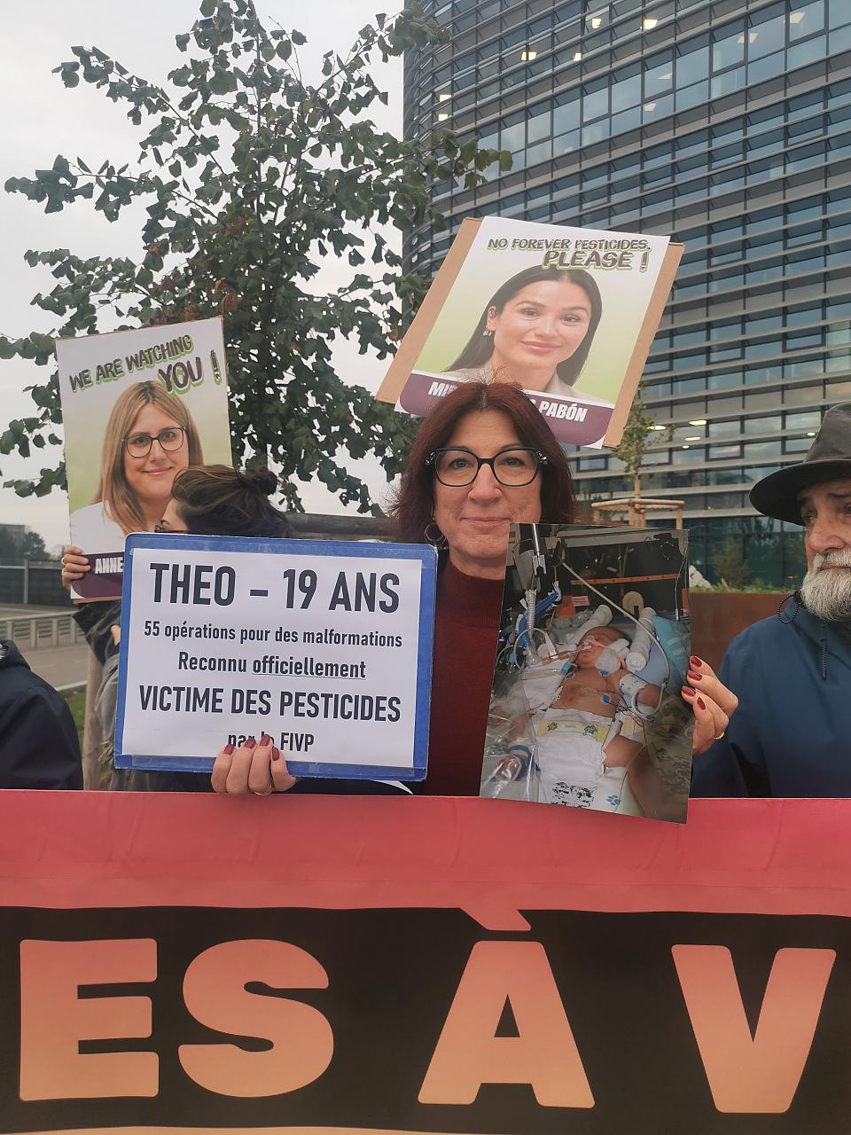 Une femme avec des lunettes porte une pancarte "théo-19 ans, 55 opérations pour des malformations, reconnu officiellement victime des pesticides par le fivp"