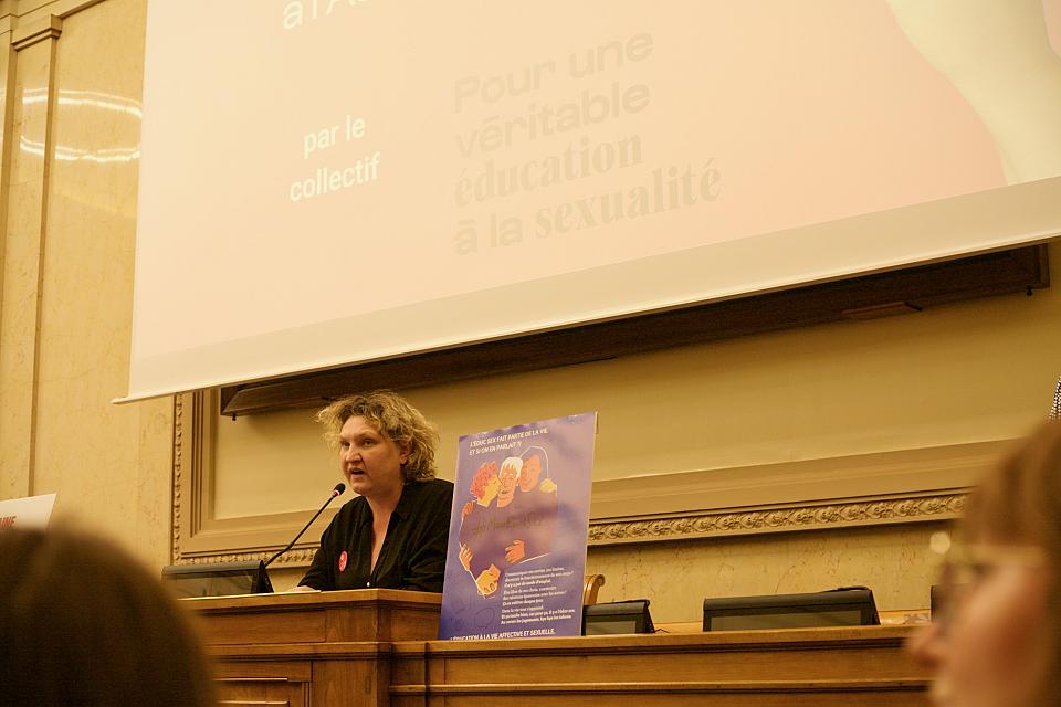 Une femme parle dans un micro derrière un bureau en bois. 