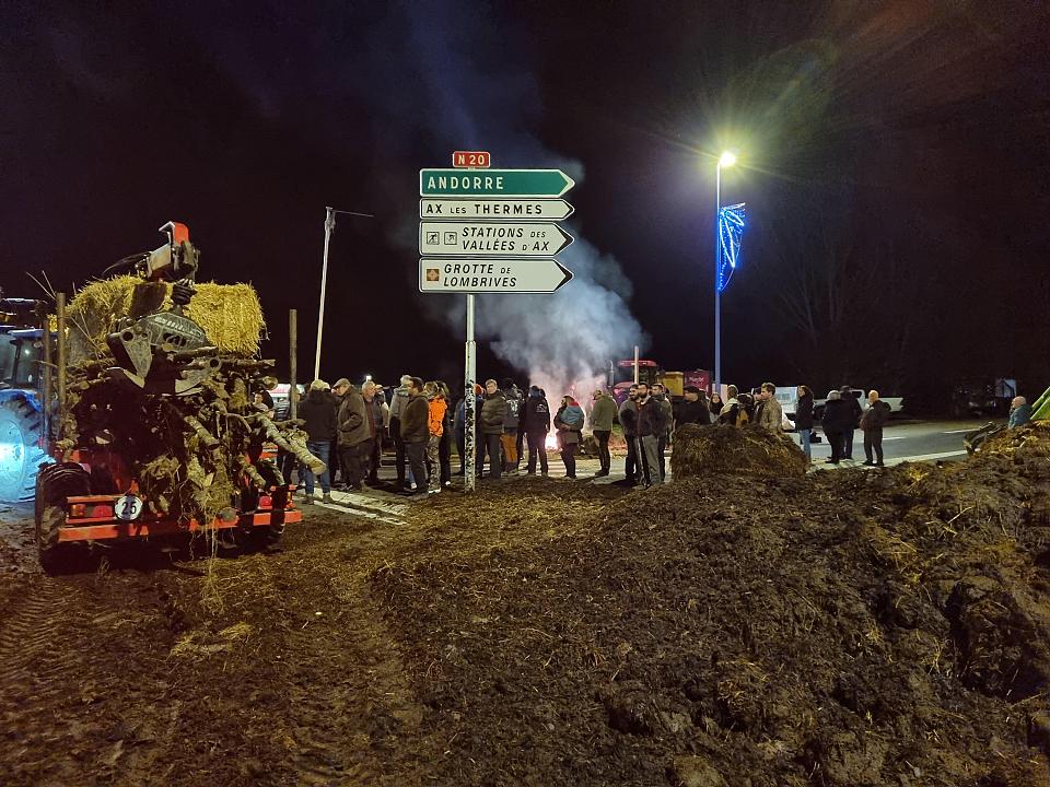 Des manifestants et un tracteur au bord d'une route de nuit, avec des feux de palettes 