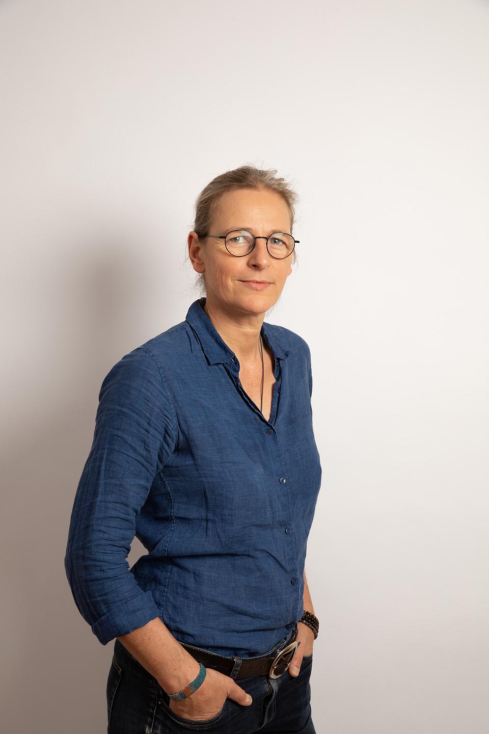 une femme vêtue d'un chemisier bleu, mais dans ses poches, regarde l'objectif