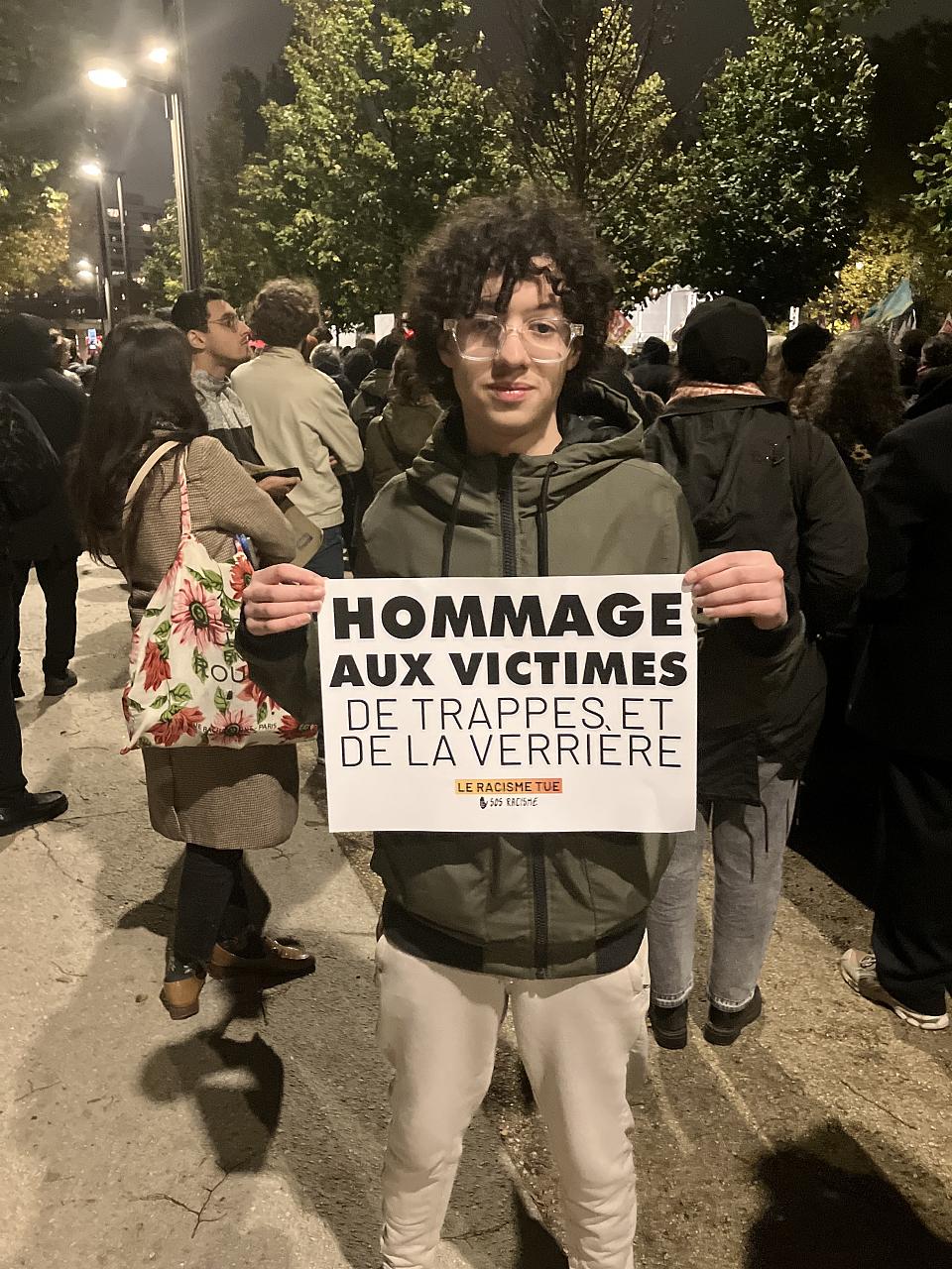 Un jeune homme tient une pancarte « Hommage aux victimes de Trappes et La Verrière ».