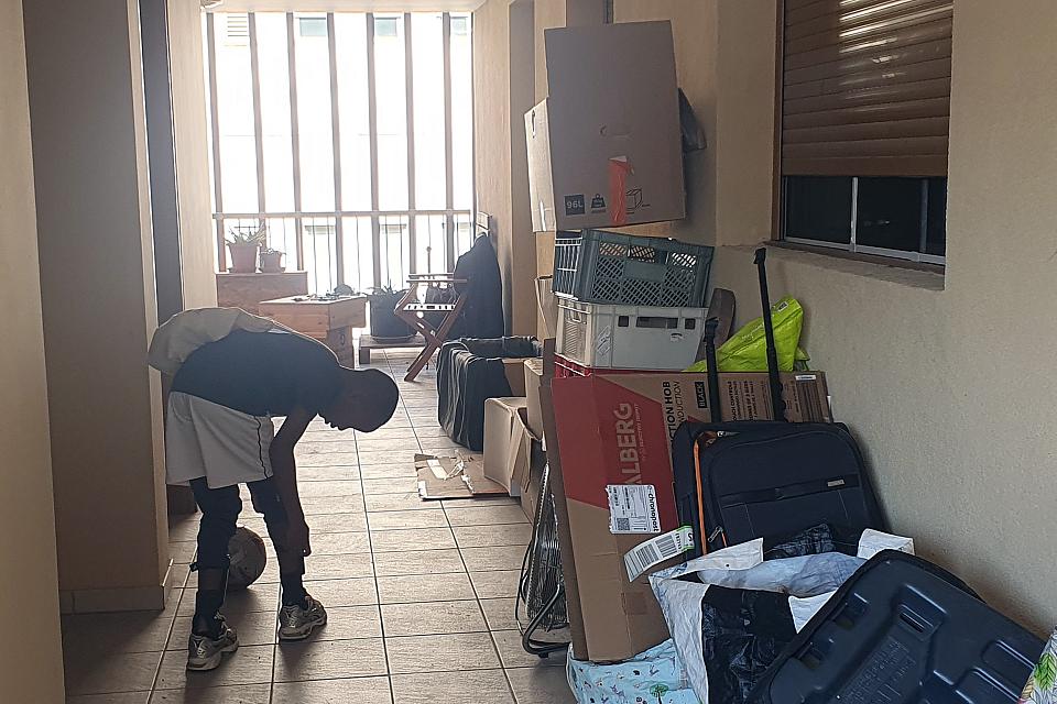 Un enfant semble lacer ses chaussures, accrocupi dans un couloir où s'entassent des affaires.