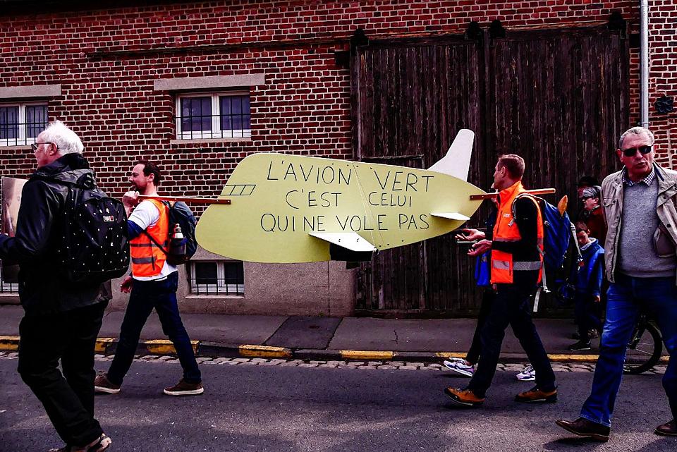 Lors d'une manifestation contre le secteur aérien, deux hommes portent une pancarte en forme d'avion sur laquelle est écrit "L'avion vert c'est celui qui ne vole pas".