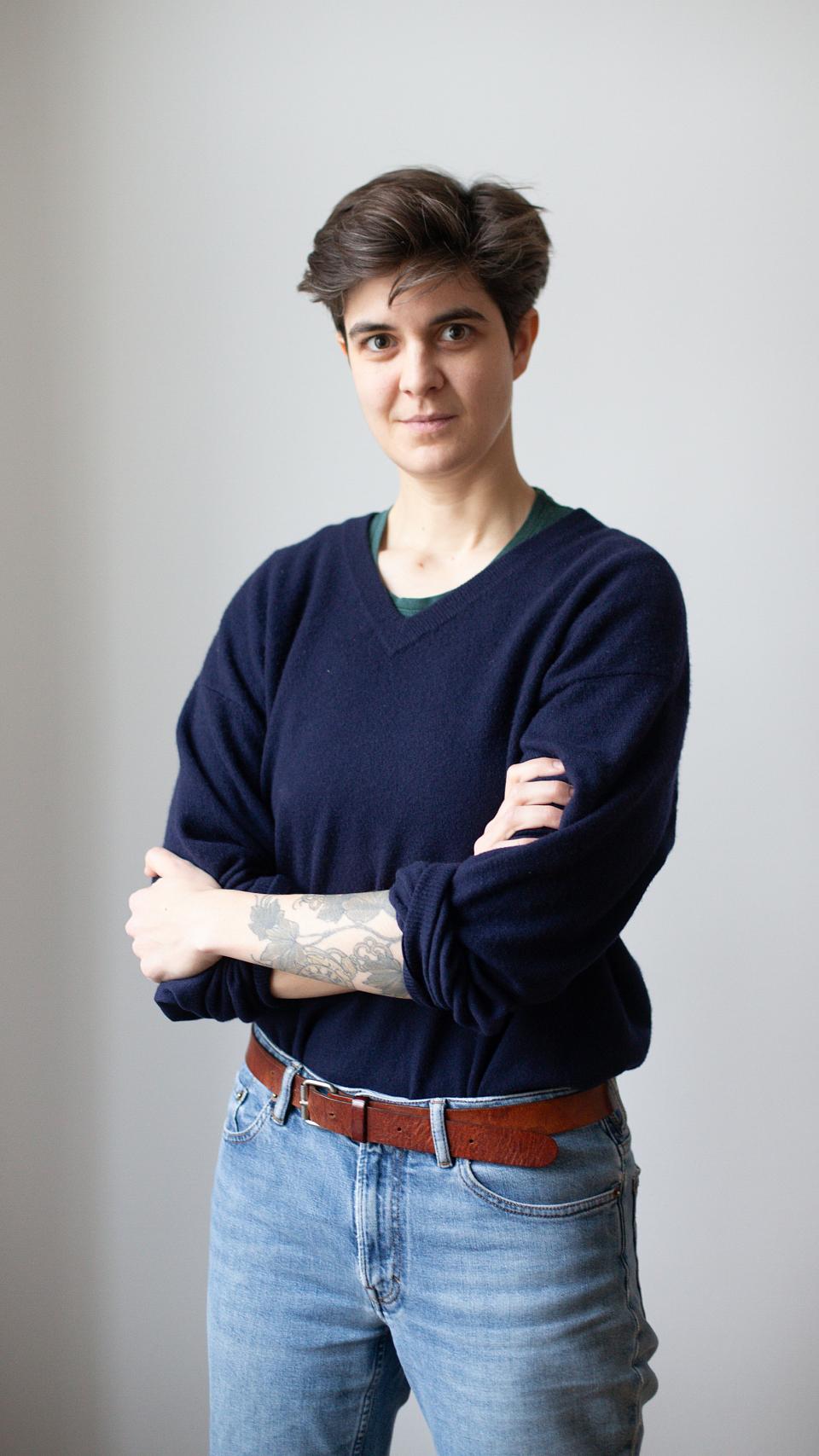 Photo de Marlene Engelhorn, debout, les bras croisés. Elle a les chevux courts, porte un jean, un pull bleu, et a un tatouage à l'avant-bras