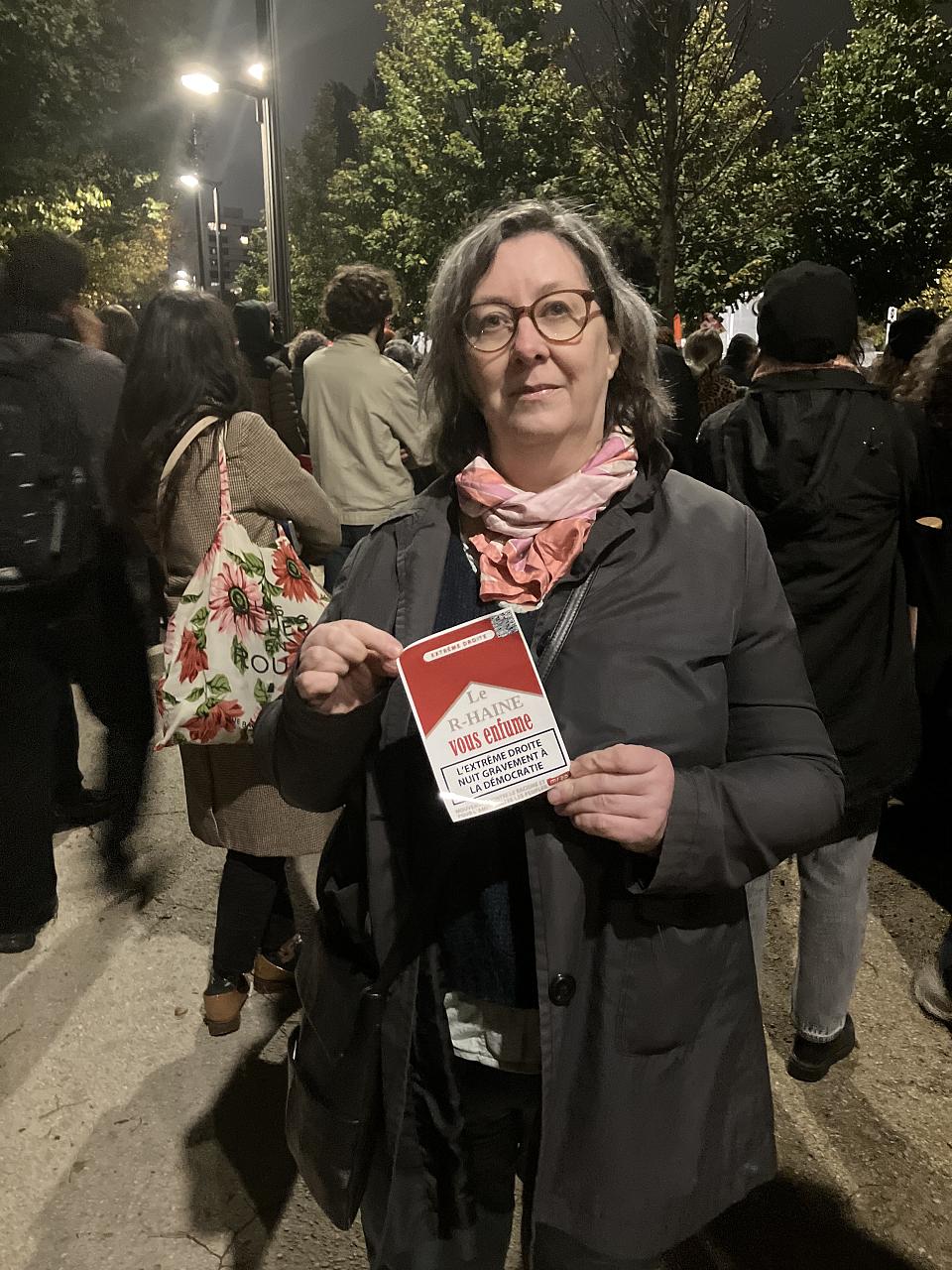 Une femme dans le rassemblement tient un carton en forme de paquet de cigarette sur lequel il est écrit « Le R-Haine vous enfume ». 