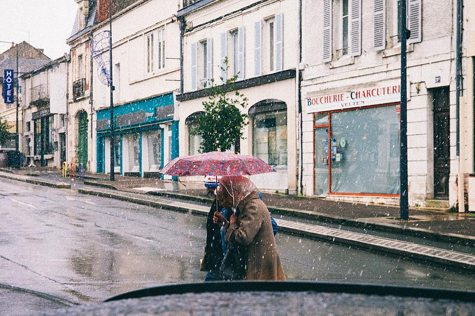 Une femme sous un parapluie traverse une rue vide. 