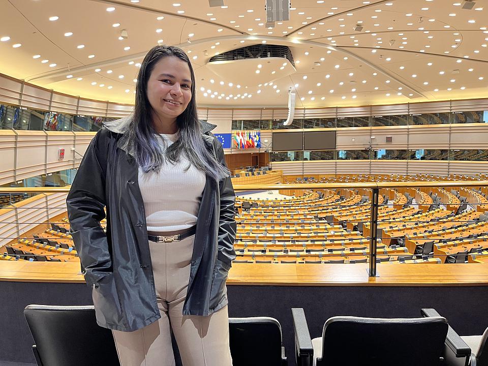 Une jeune femme sourit se tient devant l'hémicycle du Parlement européen à Bruxelles