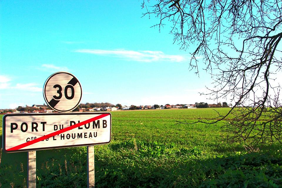 panneau à la sortie d'une commune, une parcelle agricole et des habitations en arrière plan