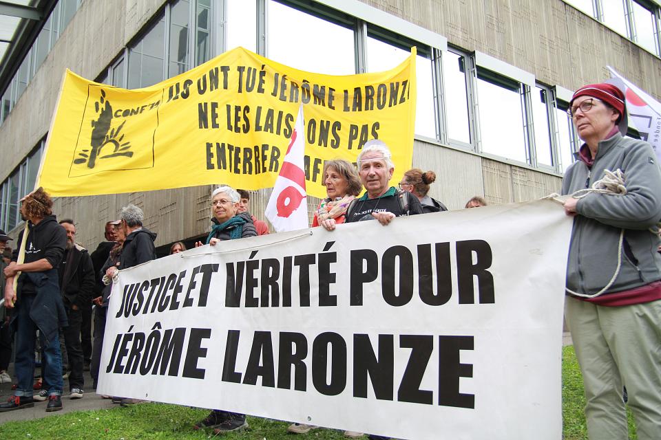 une banderole "justice et vérité pour Jérôme Laronze" est tenue pat plusieurs personnes. Derrière eux se dessine une autre banderole, jaune : "ils ont tué Jérôme Laronze, ne les laissons pas enterrer l'affaire" avec le logo de la Confédération paysanne.
