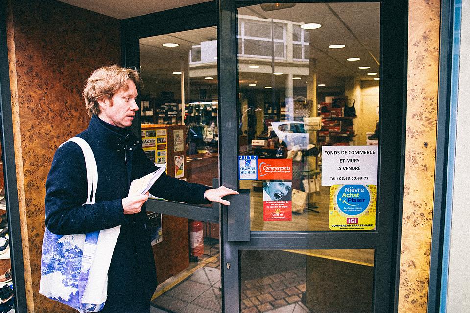 Un homme pousse la porte d'un magasin des tracts à la main. 