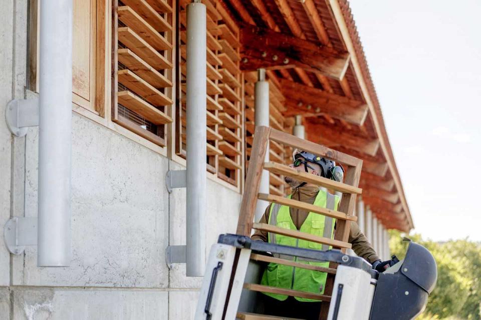 un agent installe des brise soleil en bois sur un établissement scolaire