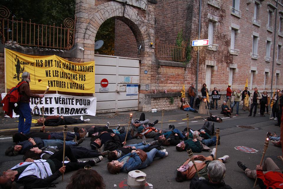 des personnes avec des flambeaux sont allongées sur le sol devant les grilles d'une gendarmerie réclamant "justice et vérité pour Jérôme Laronze"