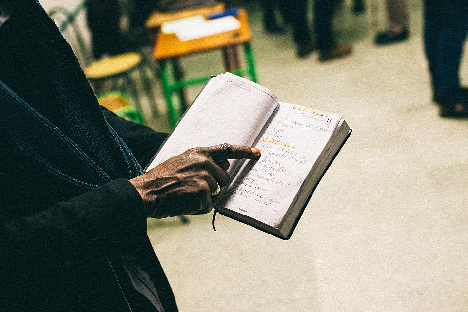 Une main d'homme pointe la page d'un cahier ouvert. 