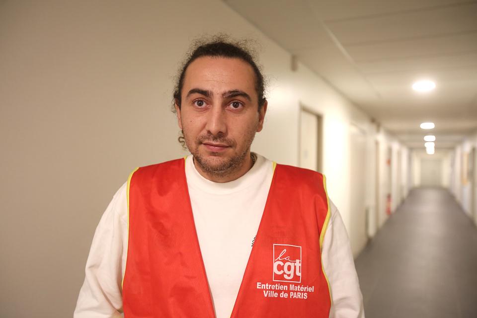 Un homme dans un couloir avec un chasuble rouge CGT. 