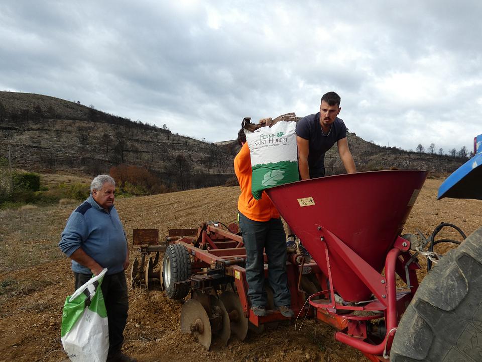 Trois hommes préparent un semoir au milieu de la garrigue.