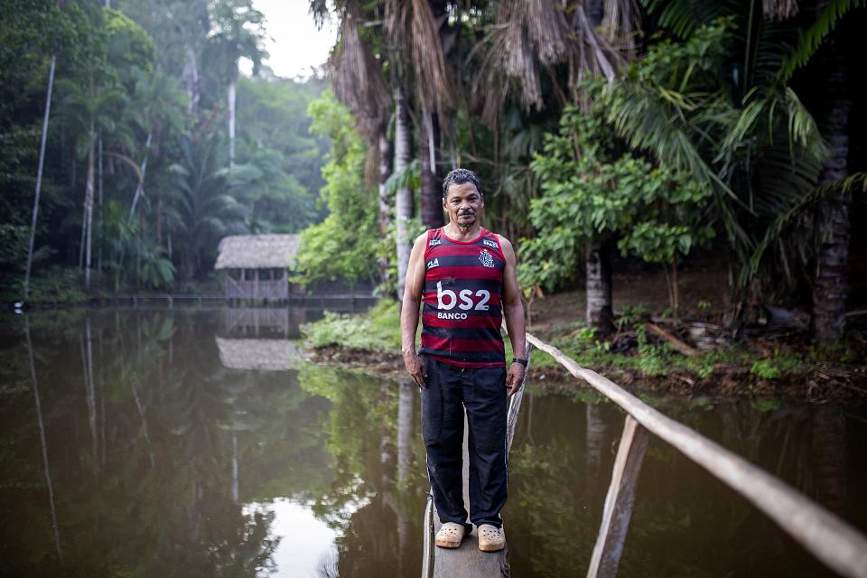 Un homme debout sur un point étroit au dessus de l'eau dans la forêt, il regarde l'objectif. 