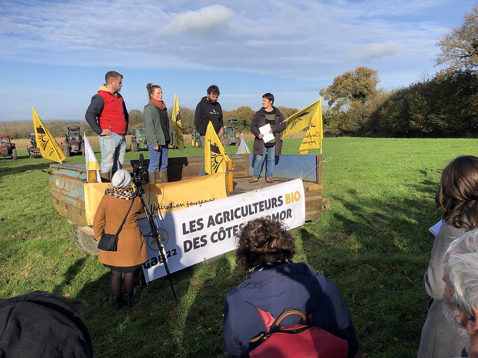 Quatre personnes prennent la parole, installées sur une remorque, entourées de drapeaux de la Confédérayion paysanne et d'une banderole du Groupement des agriculteurs bio de Côtes d'Armor