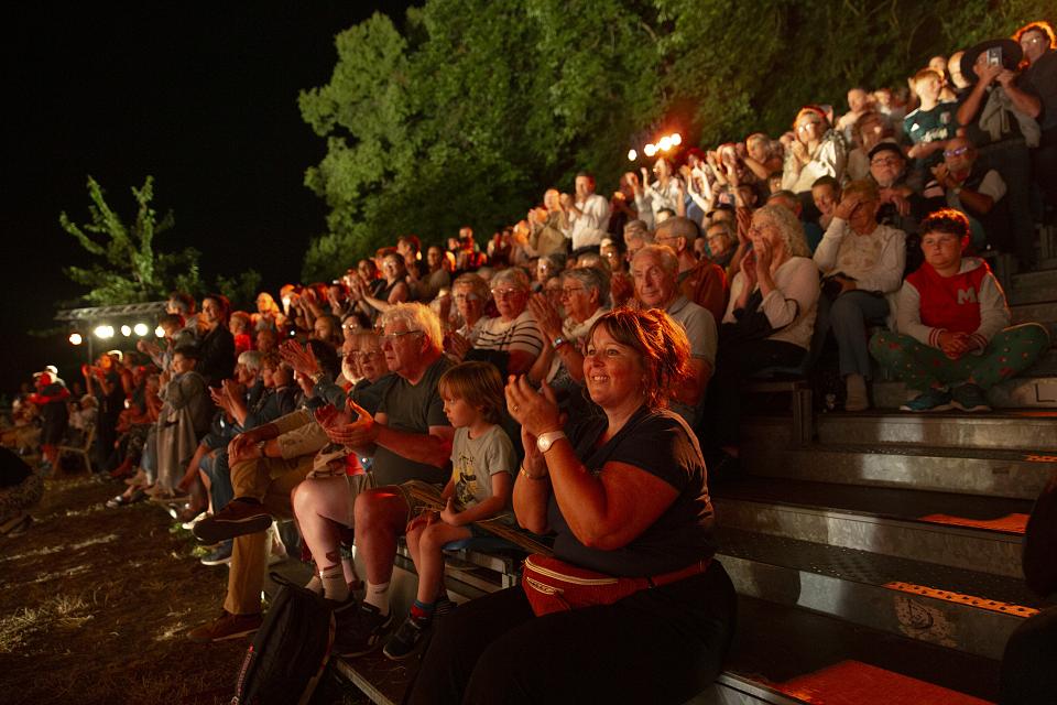Le public, assis sur des estrades en plein air et applaudissant le spectacle