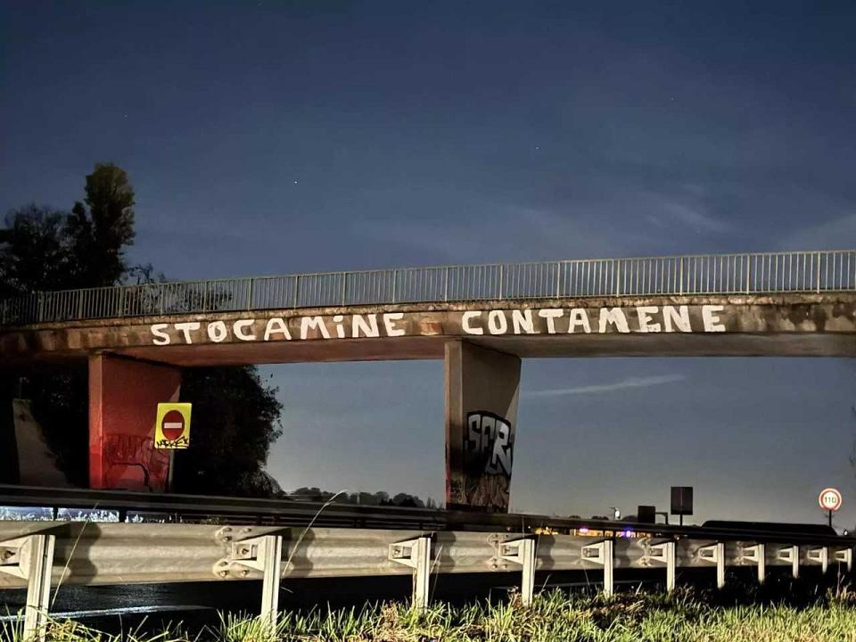 "stocamine contamene" est peint en lettre blanches sur un pont au dessus d'une voie routière