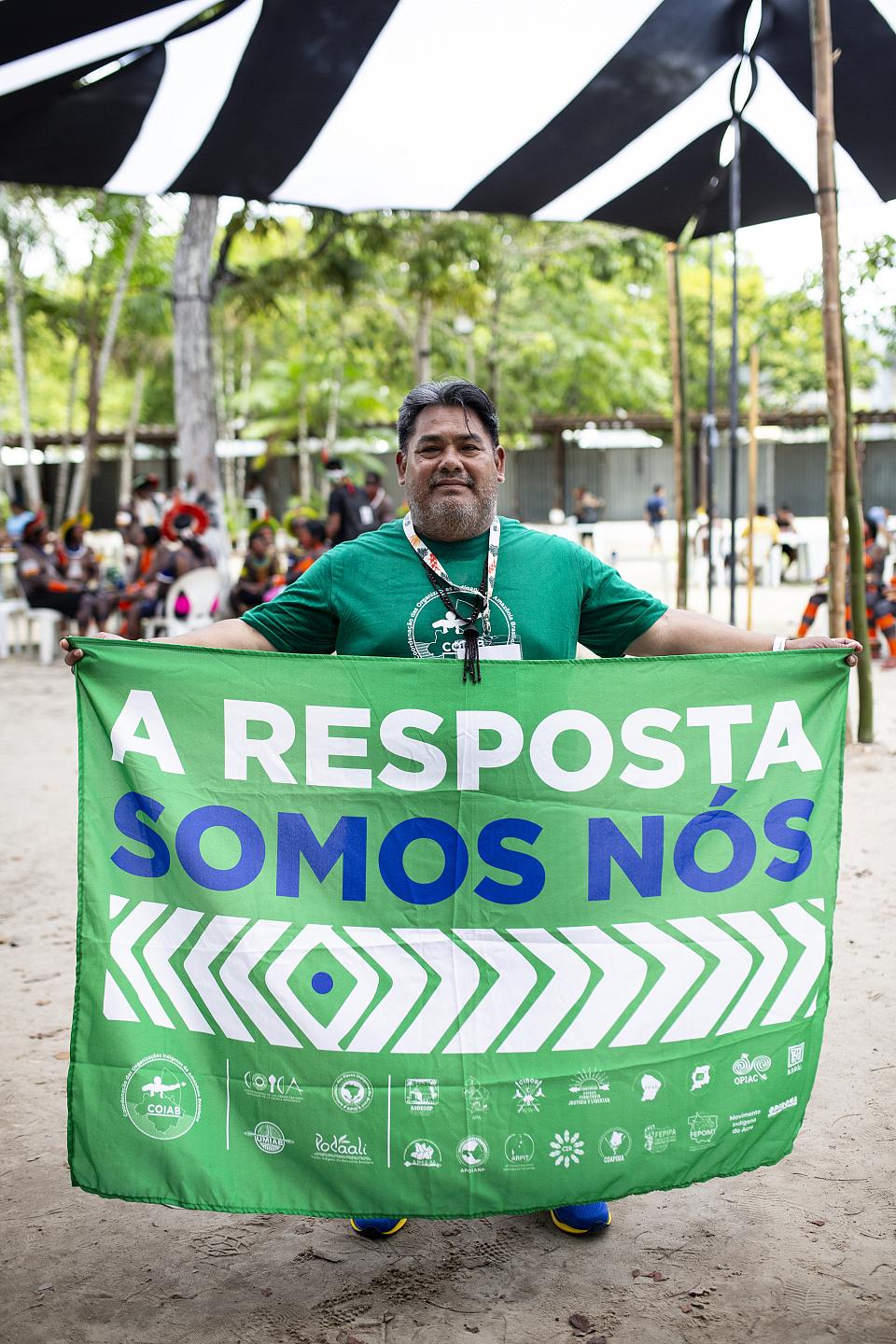 Un homme debout en t-shirt vert tient une banderole sur laquelle il est écrit « A resposta somos nos ». 