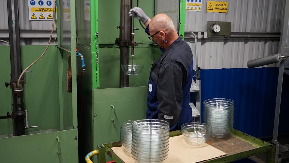 Un homme produit des saladiers en verre sur une machine 