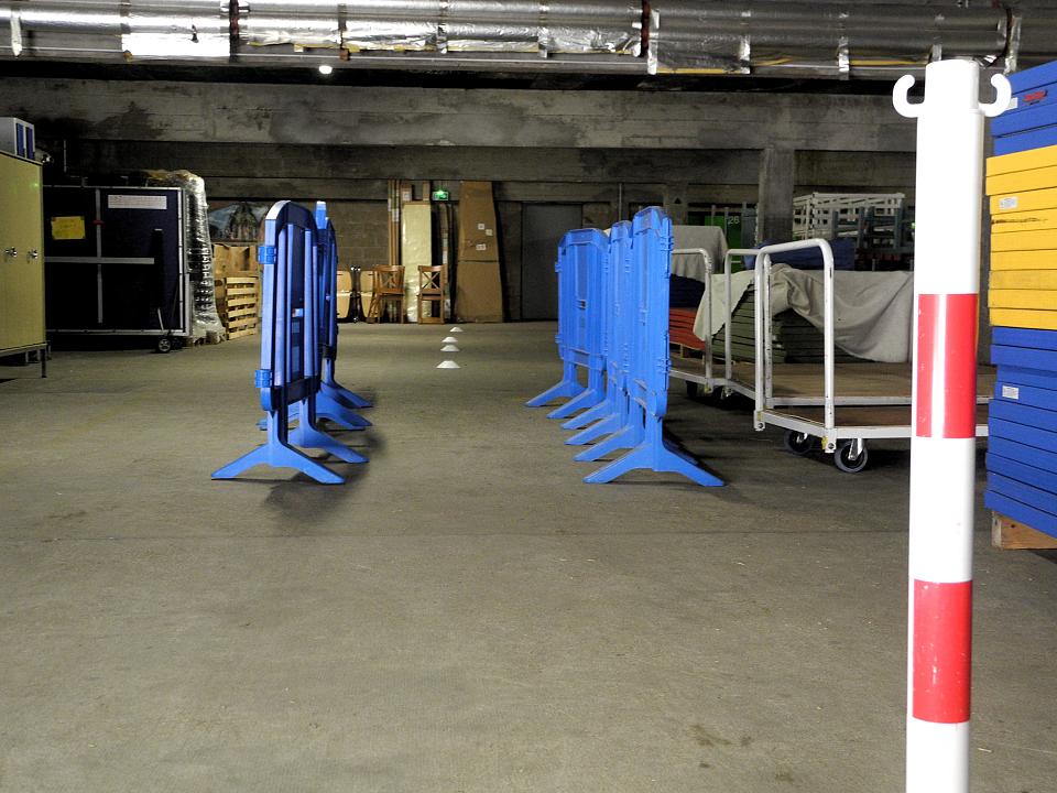 Dans un garage en sous-sol, des plots blancs sont disposés en ligne derrière des barrières bleues.