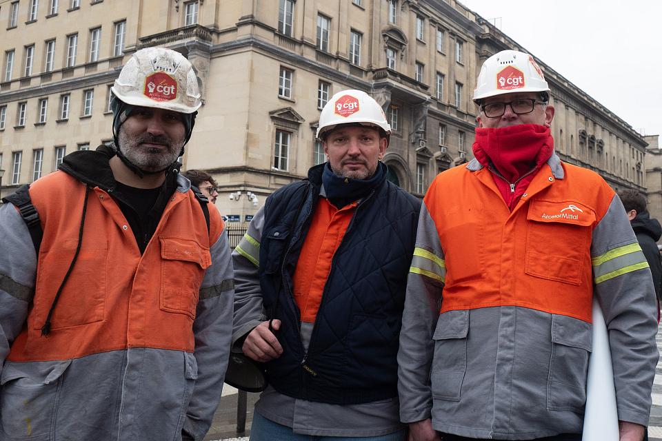 Trois hommes en habit de travail et coiffé d'un casque de travail devant un bâtiment parisien.