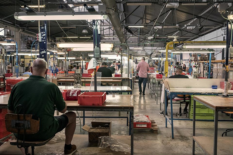Vue d'un atelier de production. Des hommes sont assis de dos à des tables devant des espace de travail.