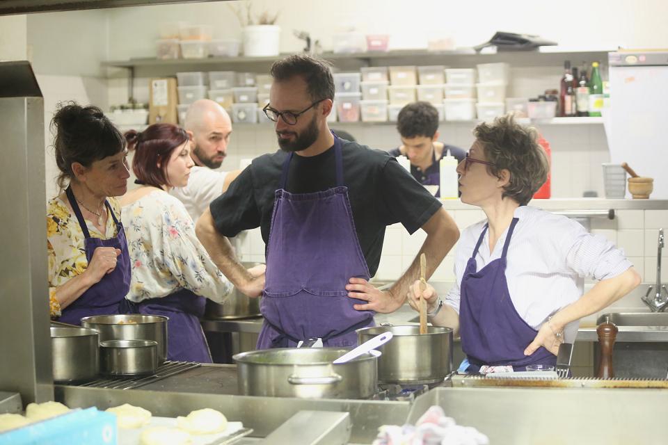 Cinq personnes en tablier dans une cuisine collective. Au premier plan, trois personnes échangent derrière des casseroles.