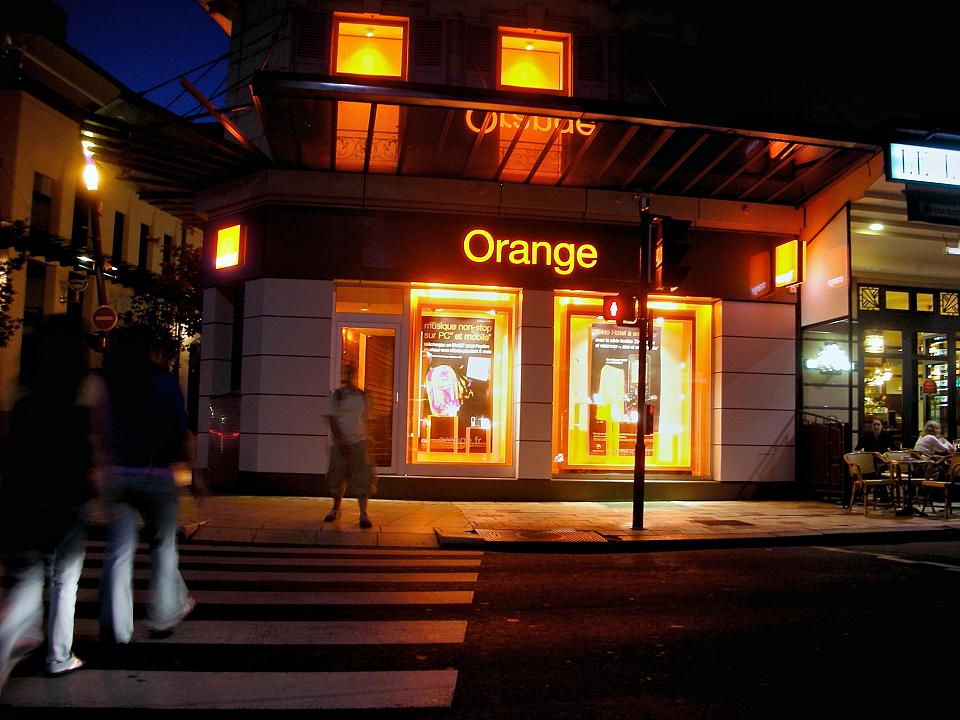 Une boutique Orange dans une ville la nuit, le nom “Orange” est illuminé en orange.