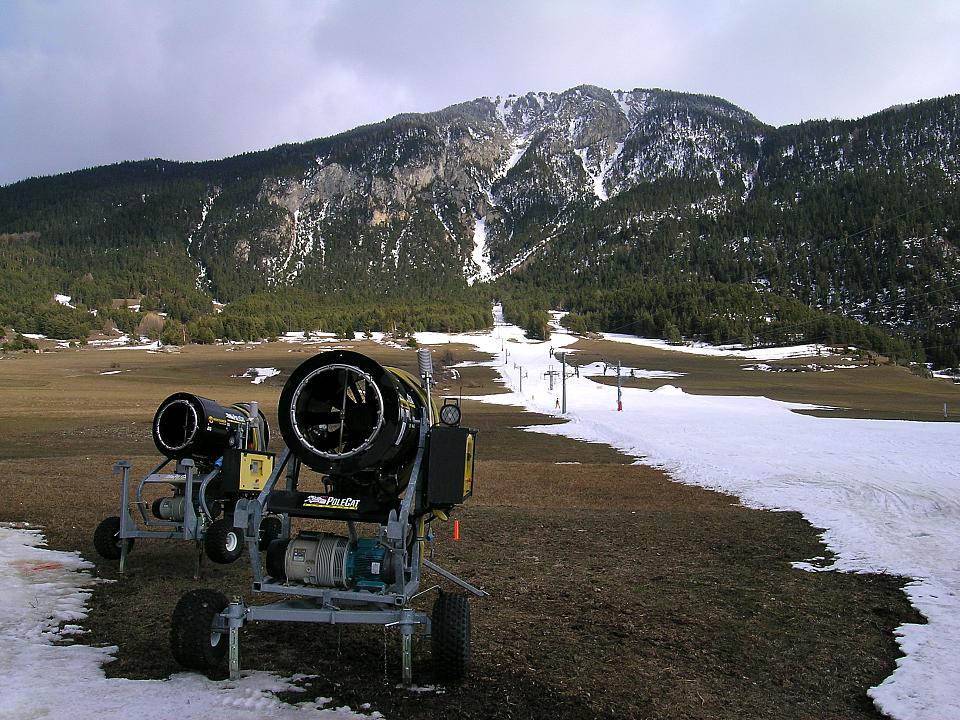 Canons à neige sur fond de paysage montagnard en manque de couverture neigeuse.