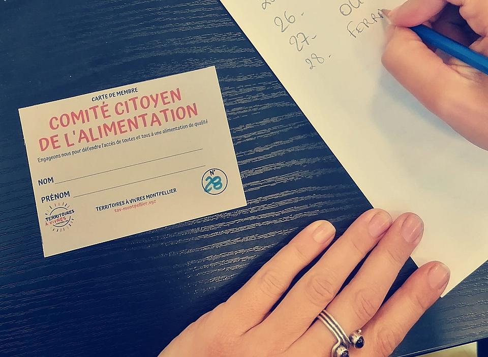 des mains écricent à côté d'une carte "comité citoyen de l'alimentation" posées sur une nappe bleue