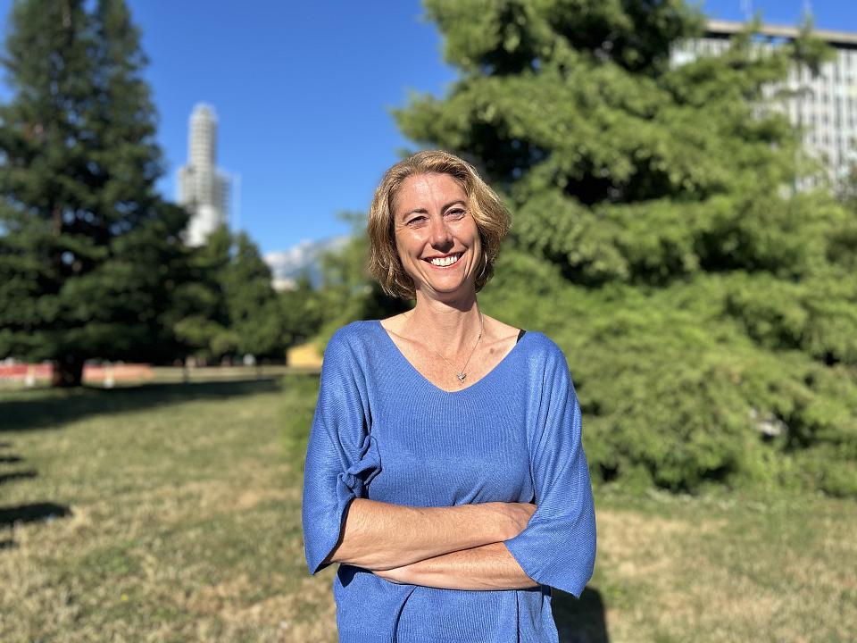 Une femme souriante croise les bras en regardant l'objectif dans un parc ensoleillé