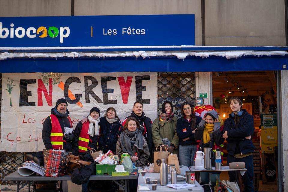 Photo de groupe des grévistes devant l'enseigne Biocoop "Les Fêtes". Ils sont neufs. Derrière eux on aperçoit une banderole "en grève". 