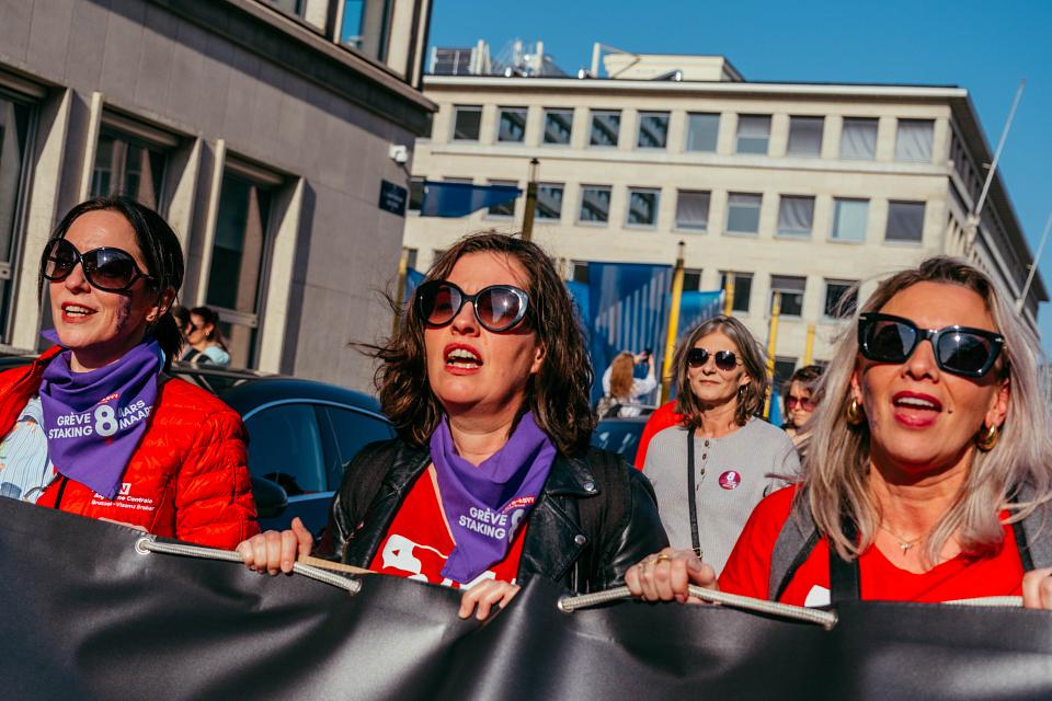 Au centre : Selena Carbonero Fernandez, secrétaire secrétaire générale de la FGTB. Elle porte un foulard violet siglé 8 mars grève féministe. Elle est entourée de deux militantes vêtues de rouges. Les trois femmes portent des lunettes de soleil.