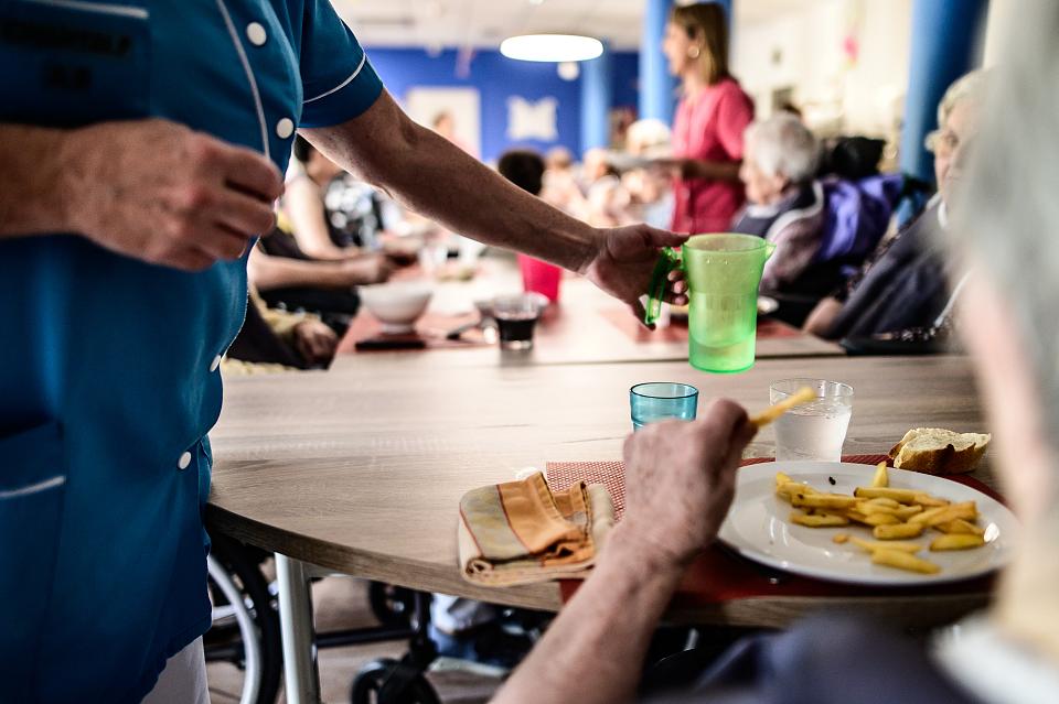 Un membre du personnel verse de l'eau a une personne âgée pendant le repas dans un Ehpad.