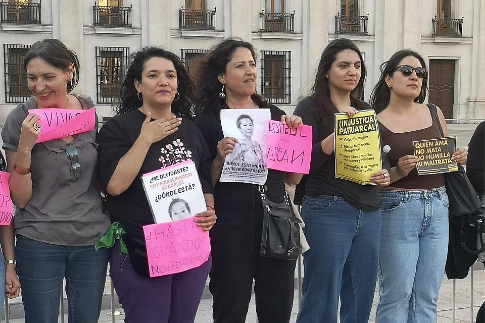 Des femmes debout dehors tiennent des feuilles sur laquelle on voit l'image d'une femme et des slogans.