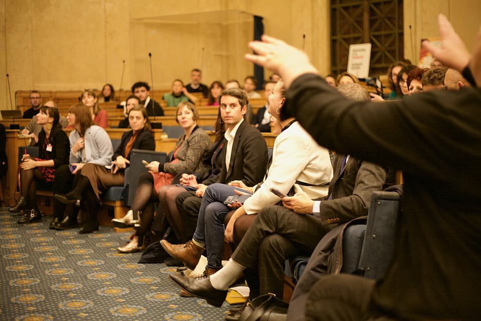 Gabriel Attal assis sur les bancs en bois d'une salle au milieu d'une vingatine d'autres personnes. 