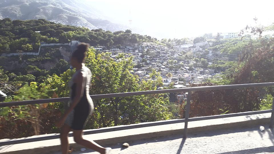 Une femme marche sur un pont devant un bidonville au loin. 