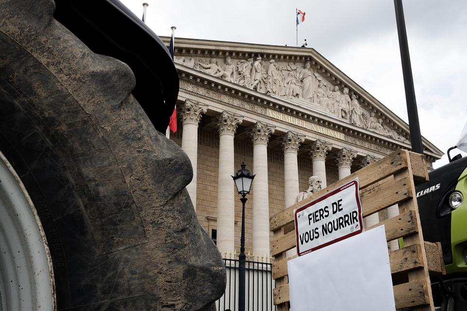 une roue de tracteur, un panneau "fiers de vous nourrir" et au fond la façade de l'assemblée nationale