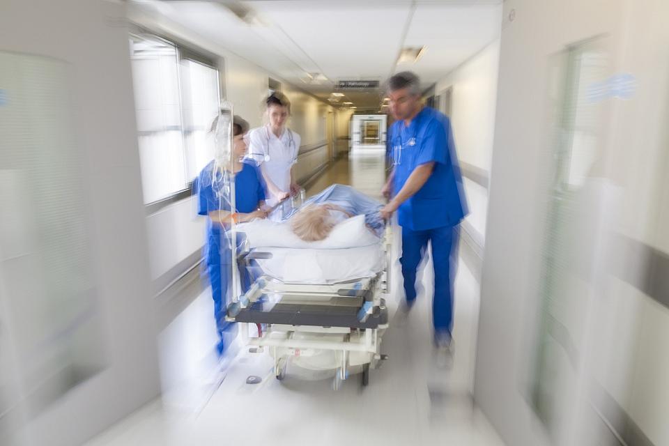 Des soignats poussent dans un couloir une personne sur un lit d'hôpital, l'image est floue.