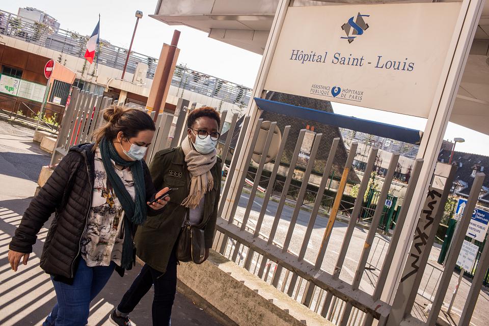 Deux femmes avec un masque passent devant l'entrée de l'Hôpital Saint-Louis. 