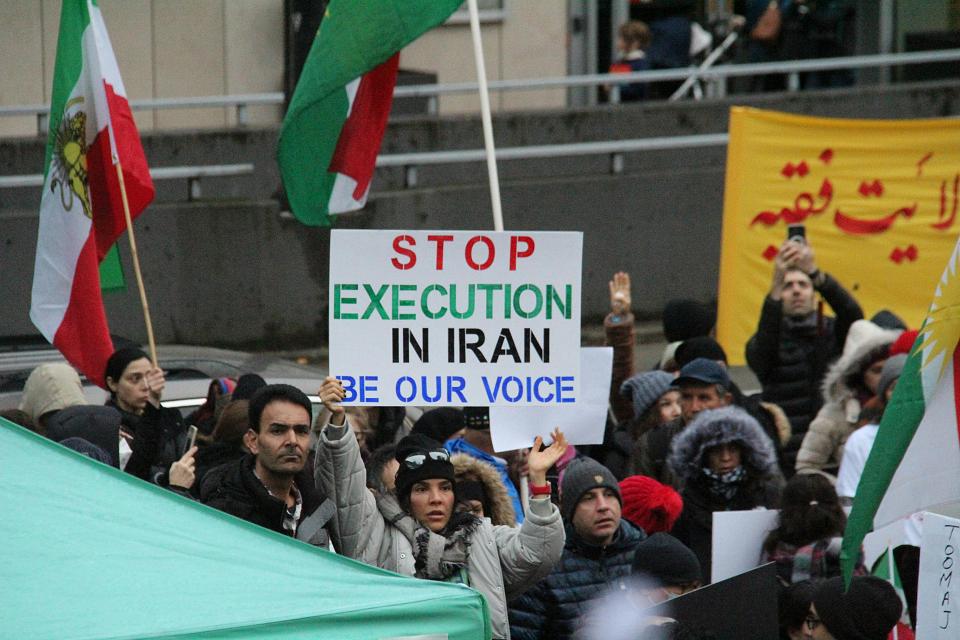 Dans une manifestation, une femme tient une pancarte sur laquelle il est écrit "stop execution in Iran, be our voice"