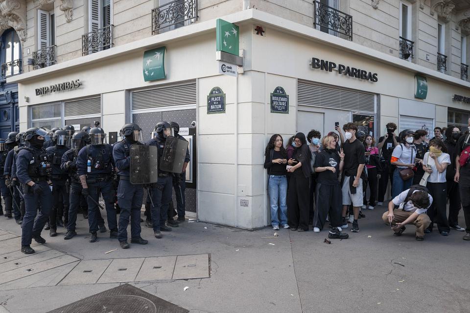 Un groupe d'une quinzaine de policiers avec casques, boucliers, matraques, juste séparé par un angle de rue d'un groupe d'une quinzaine de jeunes manifestants, Place de la Nation.